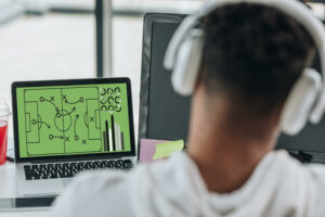 back view of african american programmer in headphones playing football video game